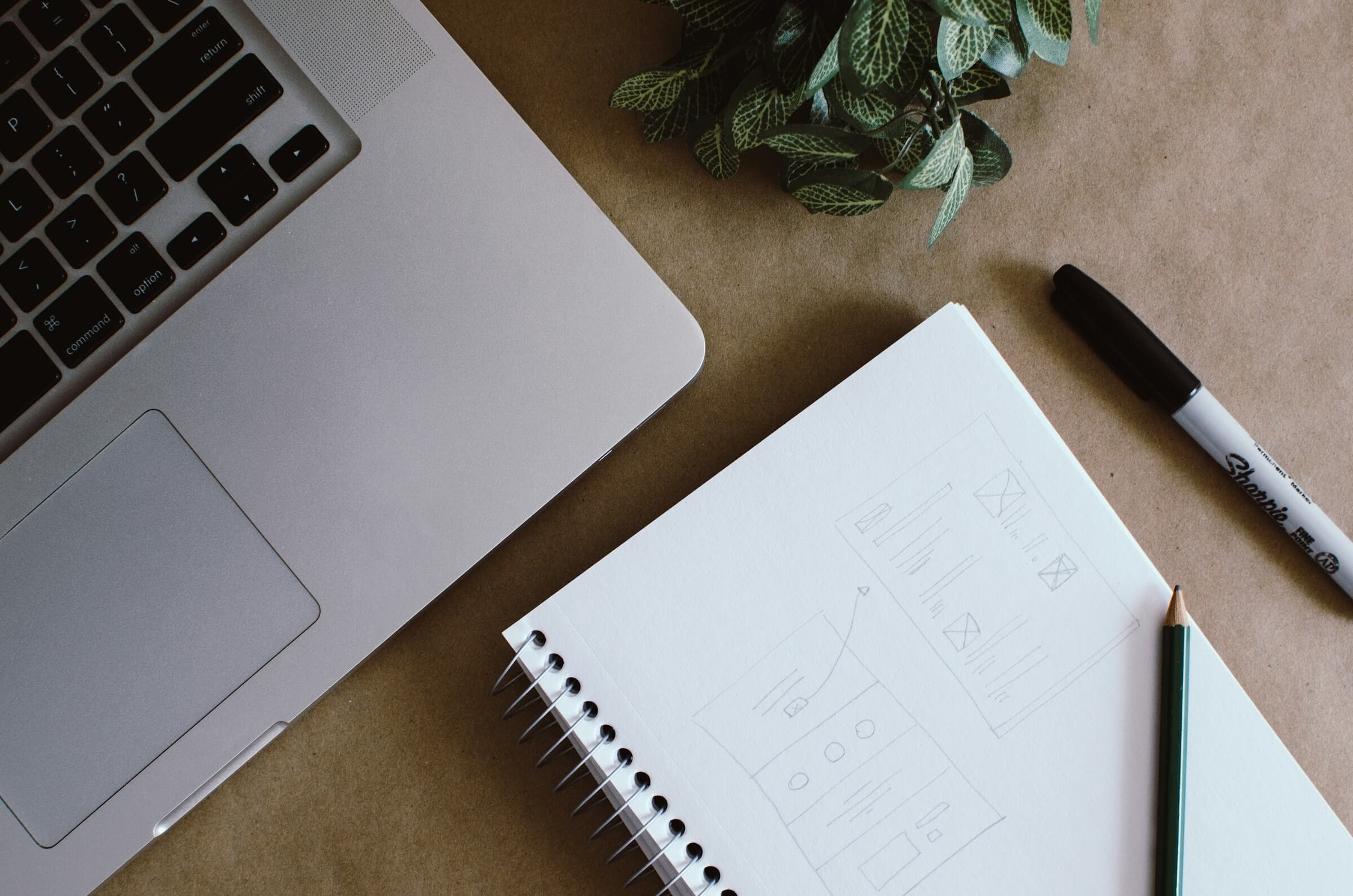 A laptop and notepad on a desk with a pencil drawing on the page, indicating meticulous planning