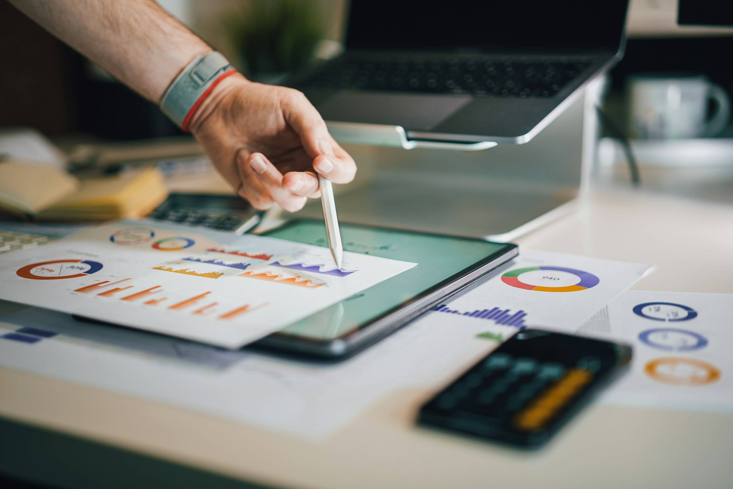 A picture of someone holding a pen against a tablet with pages of graphs sitting on top